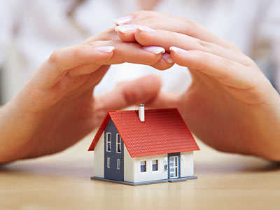 Ein Mensch beschützt ein Modellhaus mit seinen Händen.